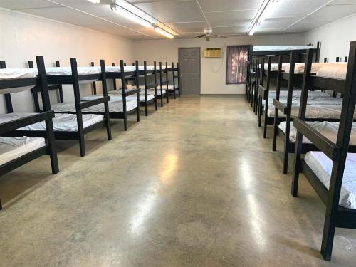 A spacious room with multiple bunk beds arranged in two rows, featuring a concrete floor and minimal furnishings.