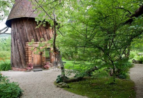 A whimsical wooden structure surrounded by lush greenery and a gravel path, creating a serene garden setting.