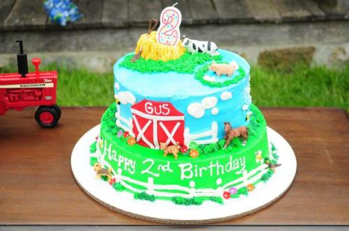 A colorful two-tier birthday cake decorated with farm animals, a barn, and a "Happy 2nd Birthday" message.
