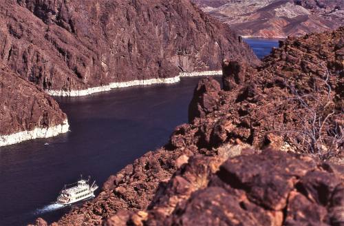 A boat navigates a winding river surrounded by rocky cliffs and arid landscapes.