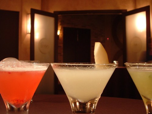 Three colorful cocktails in elegant glasses, with a blurred background of a stylish bar setting.