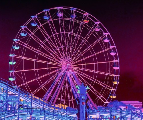 A brightly lit Ferris wheel at night, featuring vibrant purple and blue colors against a dark sky.