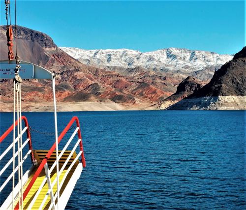 A view of a lake with a boat dock and snow-capped mountains in the background under a clear blue sky.