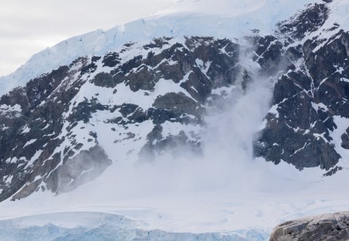 A snowy mountain landscape with a small avalanche cascading down rocky slopes.
