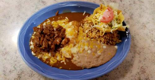 A blue plate with rice, refried beans, beef in sauce, and a taco topped with lettuce and tomato.
