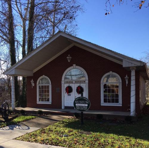 A brick building with a sloped roof, decorated for the holidays, featuring a sign that reads "C. Grado Museum."
