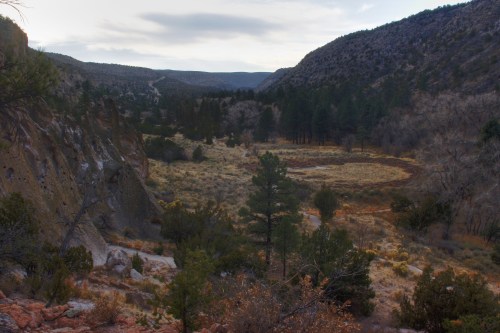 A scenic valley surrounded by mountains, featuring sparse trees and a winding path through the landscape.