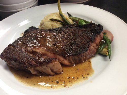 A perfectly cooked steak with a rich sauce, served with mashed potatoes and sautéed green beans on a white plate.