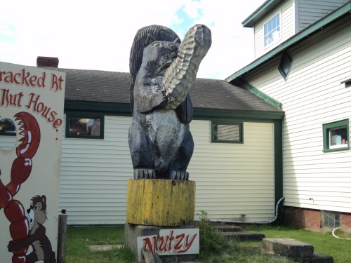 A large wooden statue of a squirrel holding a fish, standing on a yellow pedestal outside a building.