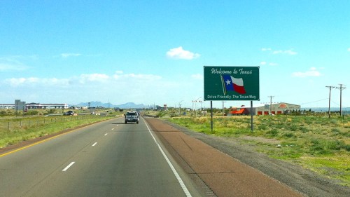 A highway sign welcomes travelers to Texas, featuring the Texas flag and a clear blue sky in the background.