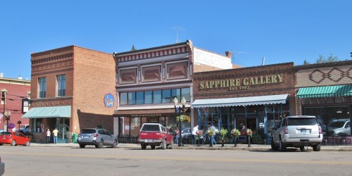 Historic buildings line a sunny street, featuring shops like Sapphire Gallery and outdoor seating.