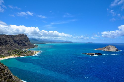 A scenic view of a coastline with turquoise waters, sandy beaches, and distant islands under a blue sky with clouds.