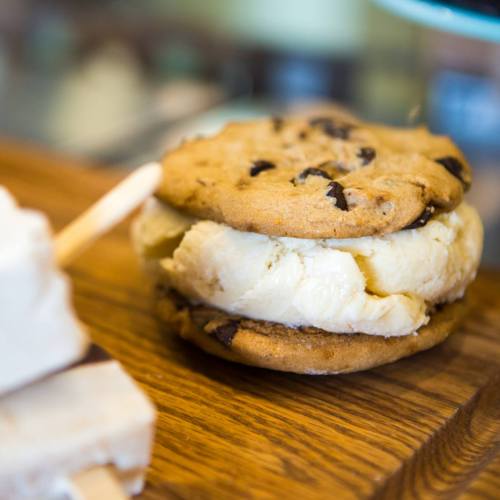 A delicious ice cream sandwich made with chocolate chip cookies and creamy vanilla ice cream, resting on a wooden surface.