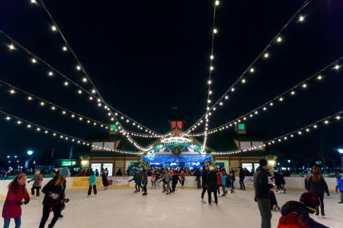 A lively ice skating rink at night, adorned with string lights and people skating joyfully.