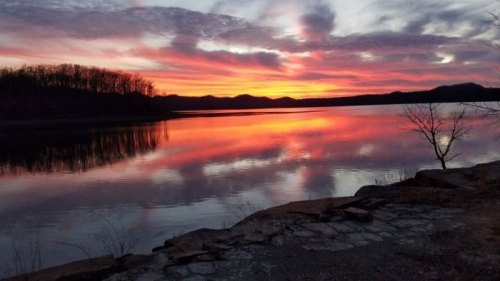 A serene sunset over a calm lake, with vibrant colors reflecting on the water and silhouettes of distant hills.
