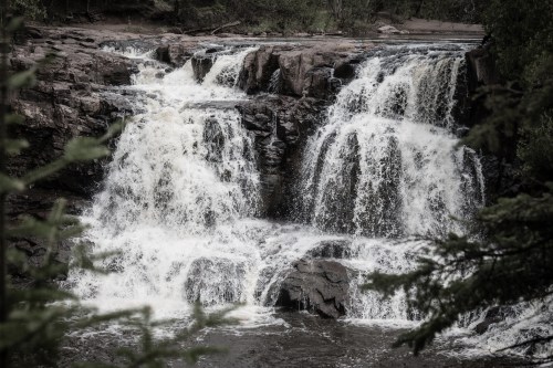 A serene waterfall cascading over rocky ledges, surrounded by lush greenery and a tranquil river.