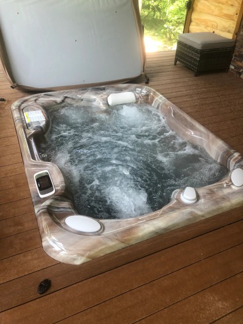 A hot tub with bubbling water, located on a wooden deck, partially covered by a lid.