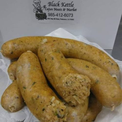 A pile of homemade Cajun sausage on a white paper, with a logo for Black Kettle Cajun Meats & Market in the background.