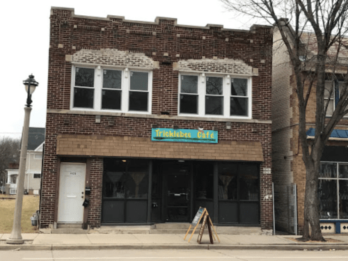 Exterior of Tricklebee Café, a brick building with large windows and a colorful sign, located on a city street.