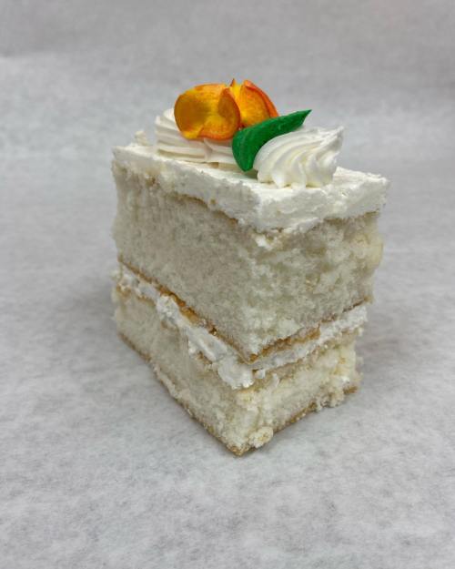 A slice of white cake with layers of frosting, topped with decorative flowers and swirls of cream.
