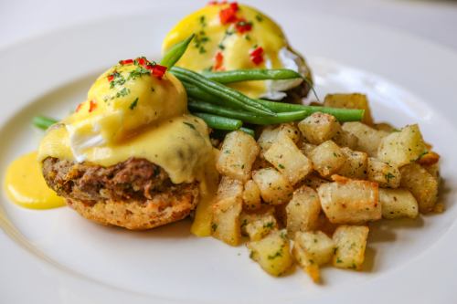 A plate featuring eggs Benedict on muffins, topped with hollandaise sauce, alongside seasoned potatoes and green beans.