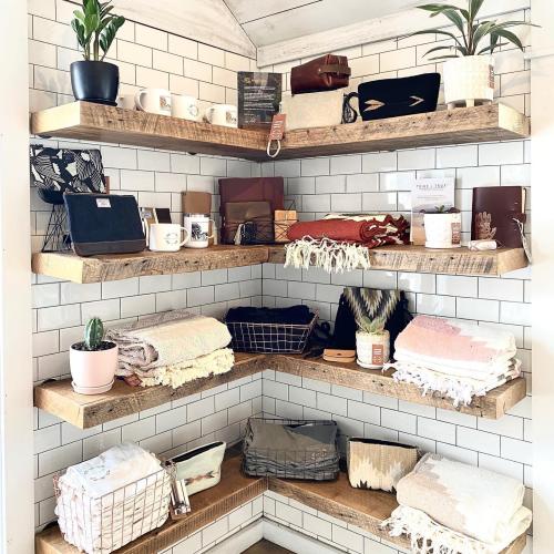 A corner display with wooden shelves featuring various home goods, including mugs, blankets, and decorative items.