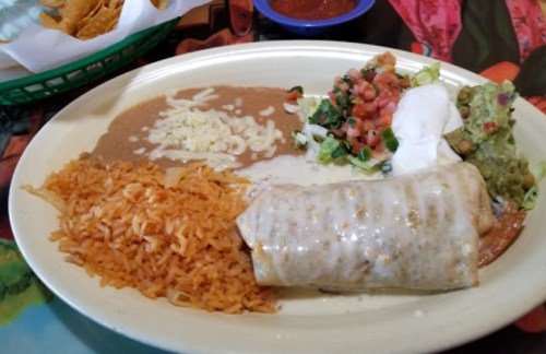 A plate of Mexican food featuring a burrito, rice, refried beans, guacamole, pico de gallo, and sour cream.