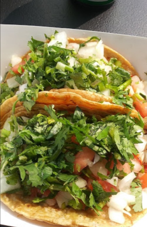 Two tacos piled high with fresh cilantro, diced onions, and tomatoes on a white tray.