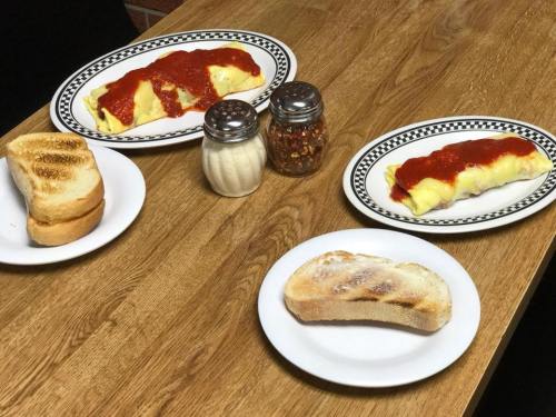 Two plates of omelets topped with red sauce, accompanied by three slices of toasted bread and condiments on a wooden table.