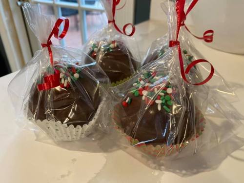 Four chocolate-covered treats in clear bags, decorated with colorful sprinkles and tied with red ribbons.