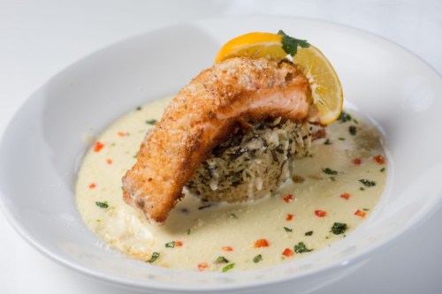 A plate featuring a crispy salmon fillet on a bed of rice, garnished with lemon and surrounded by a creamy sauce.
