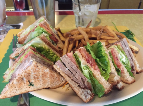A plate of stacked sandwiches with lettuce, tomato, and meat, served with a side of crispy fries.
