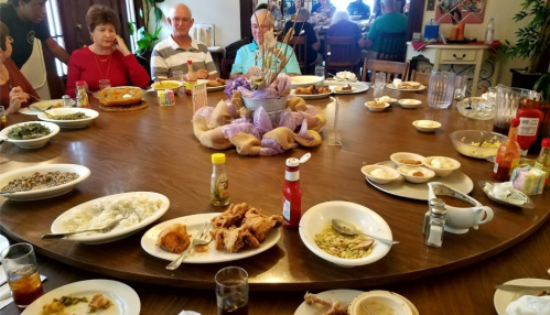 A round table set with various dishes, including rice, fried chicken, and sides, with people enjoying a meal together.