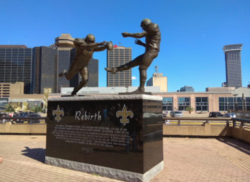 Statue titled "Rebirth" depicting two football players, with a city skyline in the background.