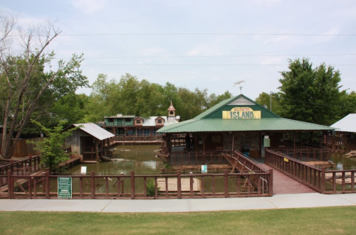 A wooden structure with a green roof, surrounded by water and trees, featuring a sign that reads "Island."