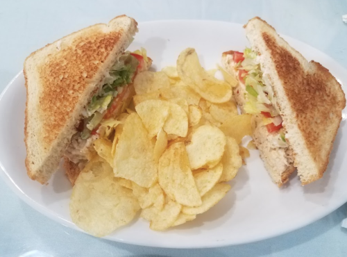 A toasted sandwich filled with lettuce, tomato, and tuna, served with a side of potato chips on a white plate.
