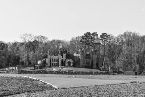 A large, ornate mansion surrounded by trees, set against a clear sky, captured in black and white.