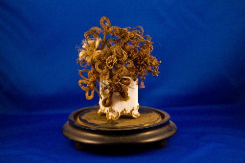 A decorative arrangement of dried flowers in a white vase, set on a dark circular base against a blue background.