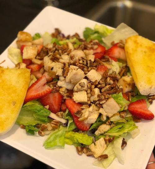 A colorful salad with lettuce, strawberries, grilled chicken, pecans, and toasted bread on a square plate.