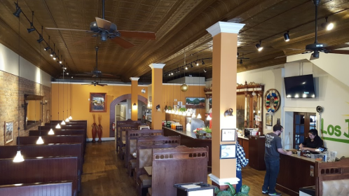 Interior of a restaurant featuring wooden booths, a bar area, and decorative elements, with staff at the counter.