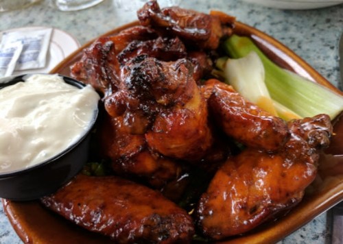 A plate of glazed chicken wings served with a side of ranch dressing and celery sticks.
