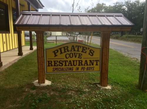 Sign for Pirate's Cove Restaurant, featuring a wooden structure and text highlighting their specialty in po-boys.