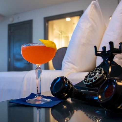 A vibrant cocktail with a lemon twist sits on a table next to a vintage black telephone in a stylish room.