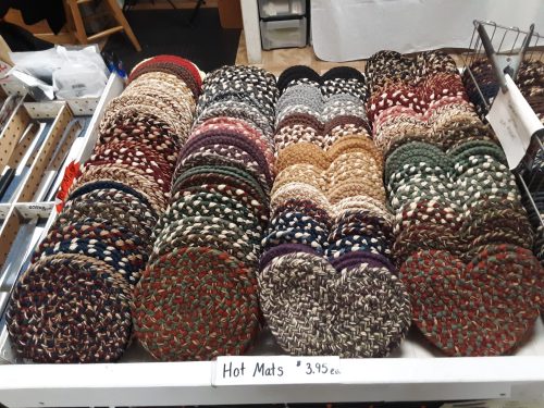 A display of colorful braided hot mats arranged neatly on a table, priced at $3.95 each.