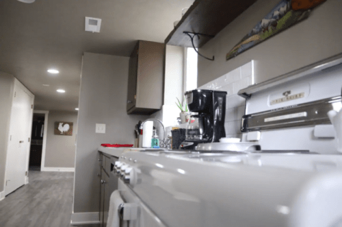 A modern kitchen with a vintage stove, coffee maker, and gray walls, featuring a view down a hallway.