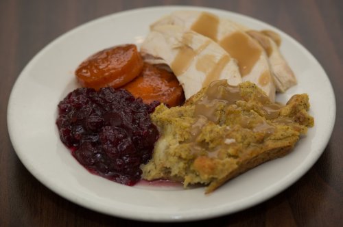 A plate with sliced turkey, gravy, sweet carrots, cranberry sauce, and stuffing.