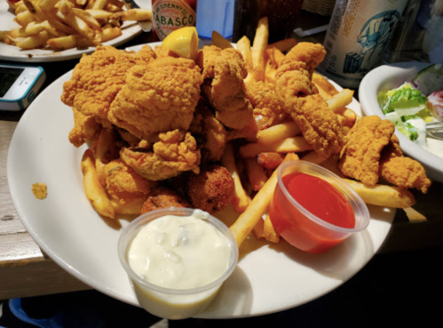 A plate of golden fried chicken pieces on a bed of French fries, served with dipping sauces.