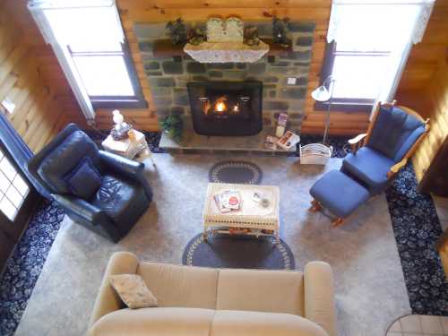 Cozy living room with a stone fireplace, two armchairs, a sofa, and a coffee table, all surrounded by wooden walls.