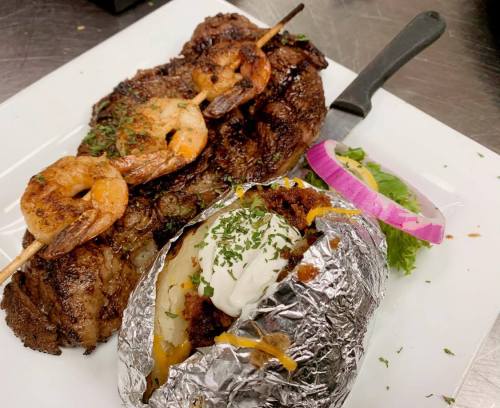 A plate featuring grilled shrimp skewers, a juicy steak, and a baked potato topped with cheese and sour cream.