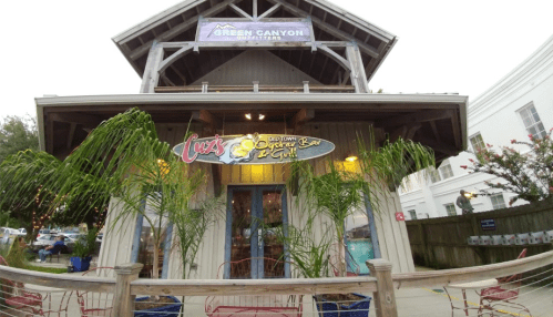 A wooden building with a sign for "Lucy's Old Town Oyster Bar & Grill" and palm plants in front.
